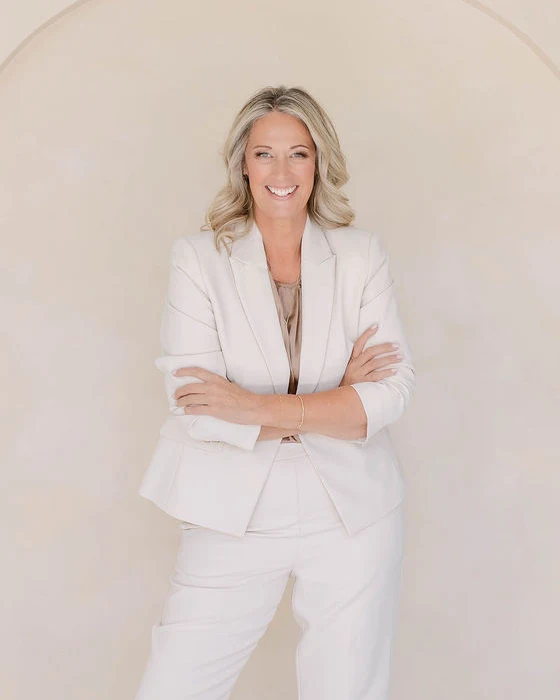 Kim Tomlinson smiling in a white suit with her arms folded.